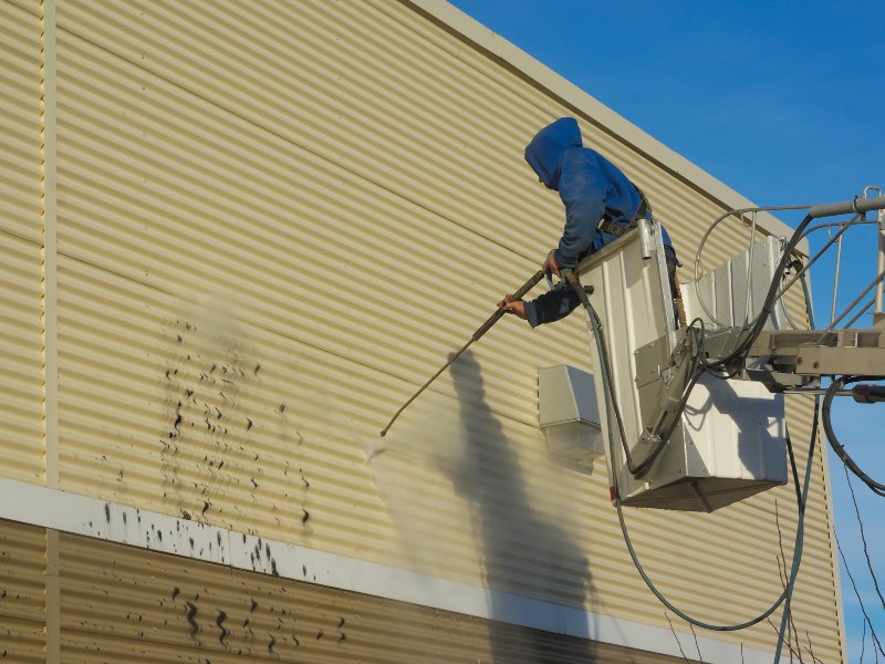 a professional using a pressure washer to clean the exterior of a building, removing dirt and grime from the walls