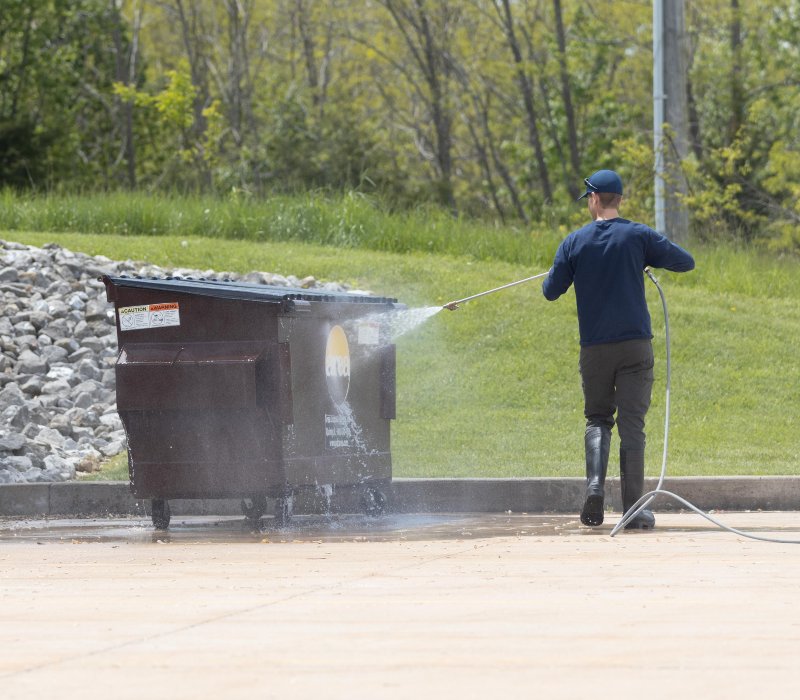 a person using a pressure washing machine to clean a green dumpster