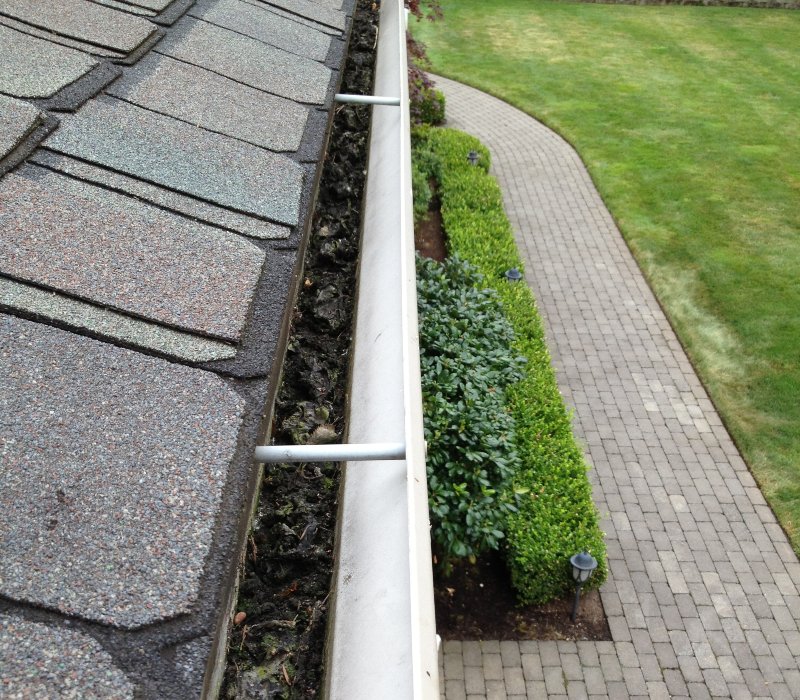 A man is cleaning a clogged roof gutter from dirt, debris and fallen leaves to prevent water damage and let rainwater drain properly