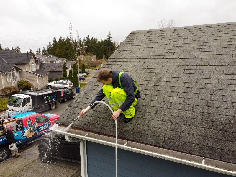 A man is cleaning a clogged roof gutter from dirt, debris and fallen leaves to prevent water damage and let rainwater drain properly