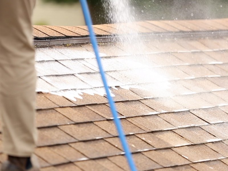 a large roof with shingles being sprayed with a cleaning solution from a hose